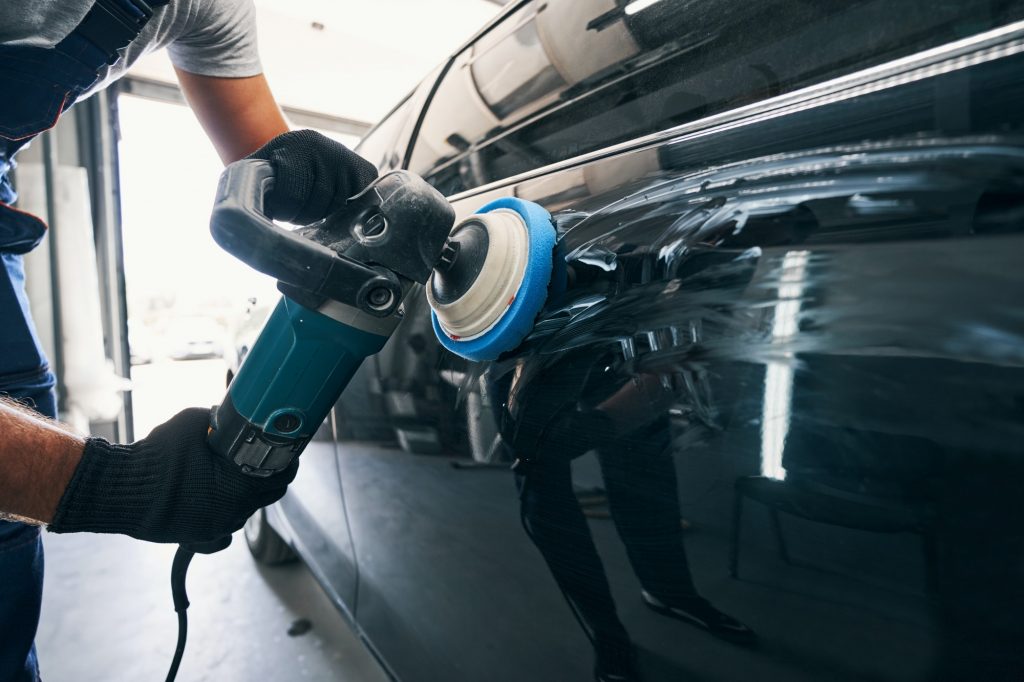 Auto mechanic using polisher with felt pad on car