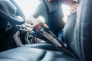 cropped view of car cleaner vacuuming drivers seat in car